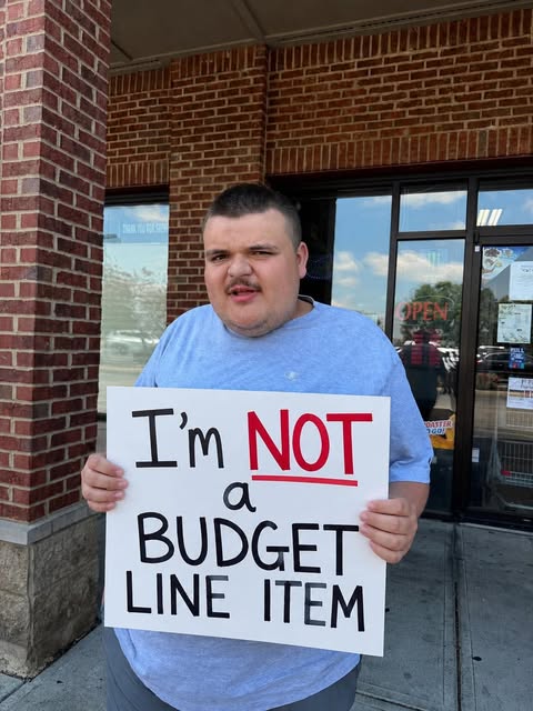 Jr. holding a sign that reads I'm not a budget line item